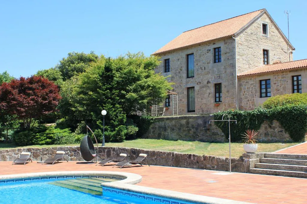 Casa señorial de piedra con piscina, tumbonas y silla colgante en el jardín, Casa A Pedreira