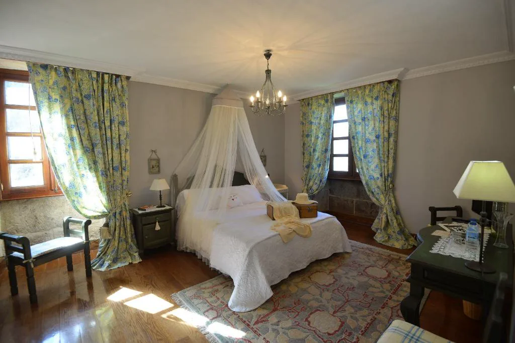 Dormitorio romántico con cama de dosel de gasa blanca y cortinas florales, Casa A Pedreira