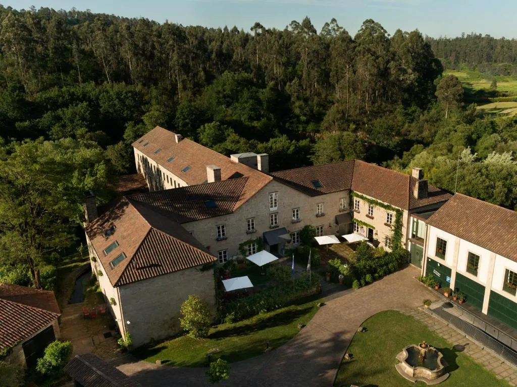 Vista aérea del conjunto del hotel rodeado de bosque junto al río Sar, con la fuente del jardín en primer plano
