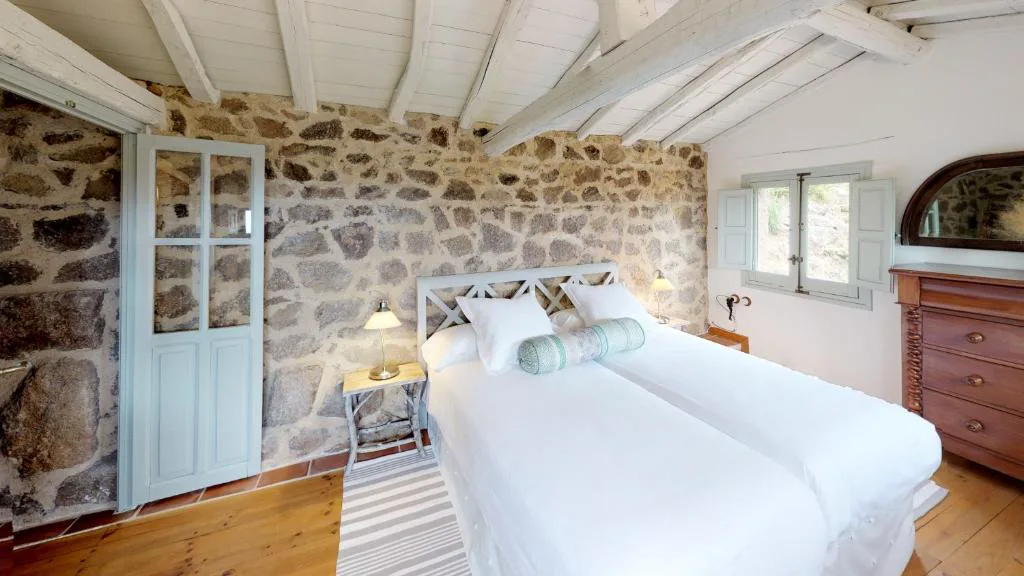 Dormitorio con cama doble, muro de piedra y cabecero blanco