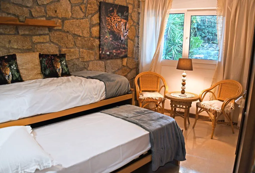 Dormitorio con muro de piedra, dos camas y sillones de mimbre