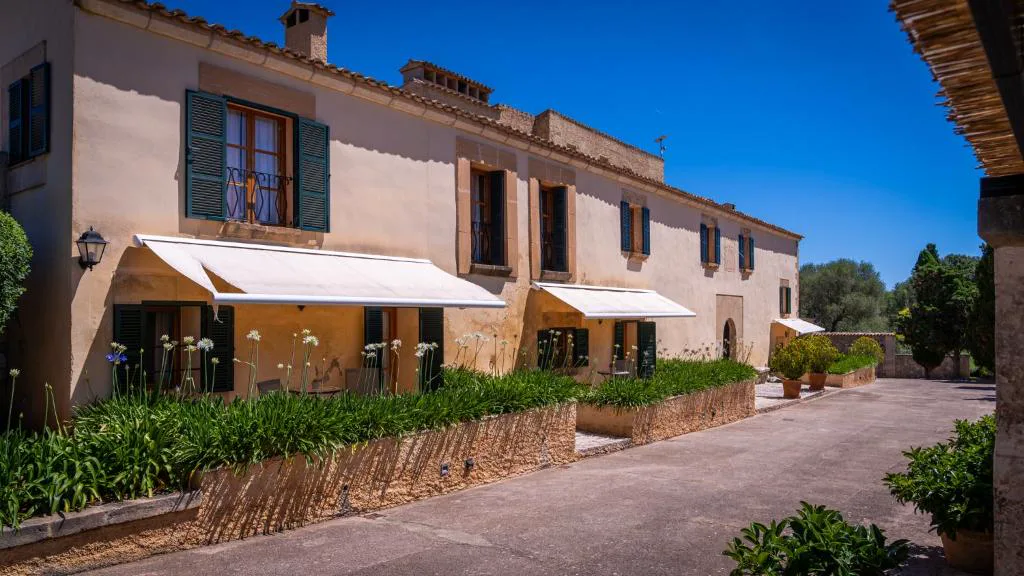 Fachada de la finca con contraventanas azules y toldos blancos entre agapantos, Agroturisme Son Cardaix