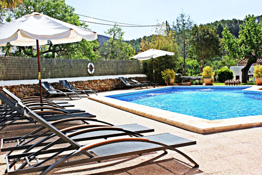 Piscina rodeada de tumbonas y sombrillas con vistas a las colinas de Sant Joan de Labritja, Agroturismo Can Fuster, Ibiza