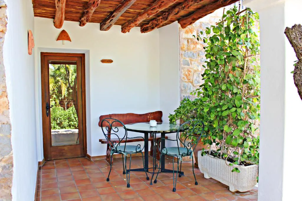 Porche con mesa de forja y enredadera junto a una puerta de madera, Agroturismo Can Fuster