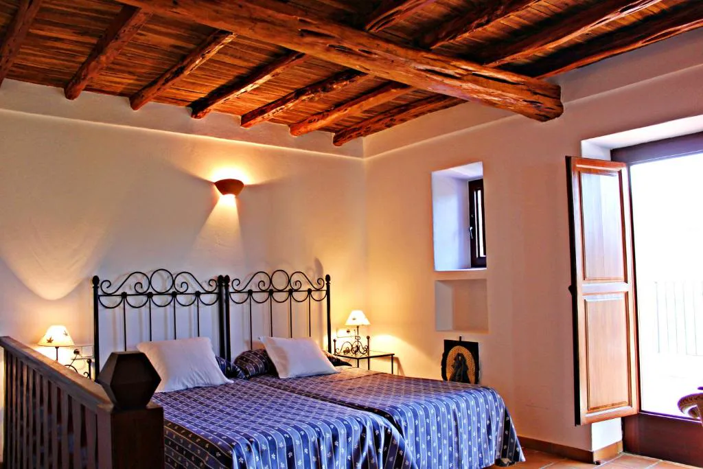 Dormitorio con dos camas y ropa de cama azul junto a un balcón con vistas al campo, Agroturismo Can Fuster