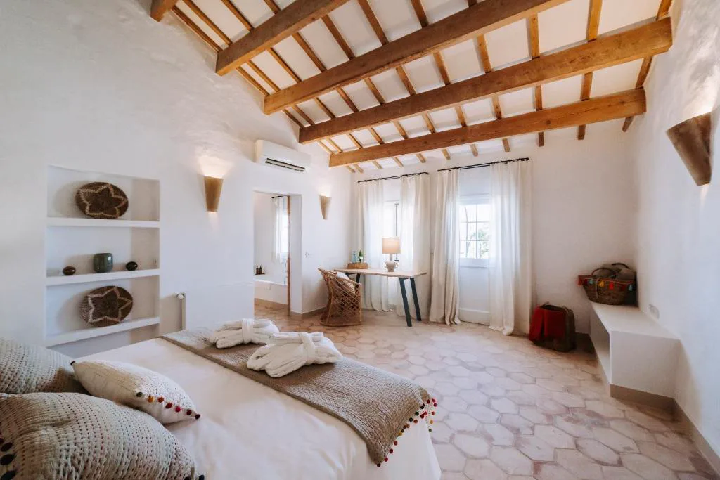 Dormitorio rústico con techo de vigas y albornoces sobre la cama, Agroturismo Rafal Rubí