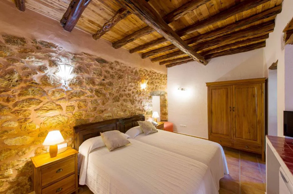 Dormitorio rústico con techo de vigas de madera y pared de piedra, Agroturismo Xarc