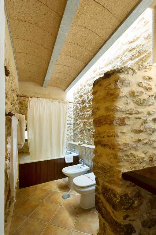 Baño rústico con bañera, cortina de tela y muros de piedra, Agroturismo Xarc