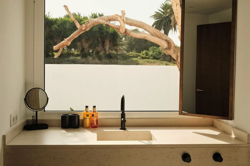 Baño con lavabo integrado y vistas al jardín a través de la ventana, Alava Suites