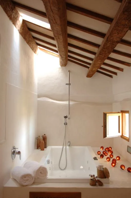 Baño con bañera bajo vigas de madera y velas encendidas alrededor, Alcaufar Vell