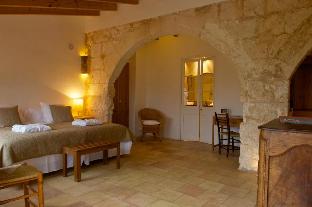 Dormitorio con arcos de piedra, escritorio antiguo y sillón de mimbre, Alcaufar Vell