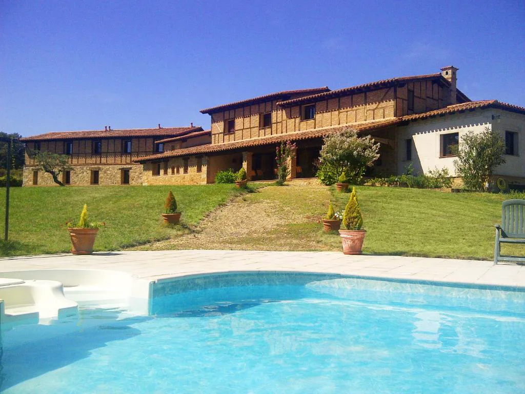 Piscina azul frente a una casa rural de piedra con jardín