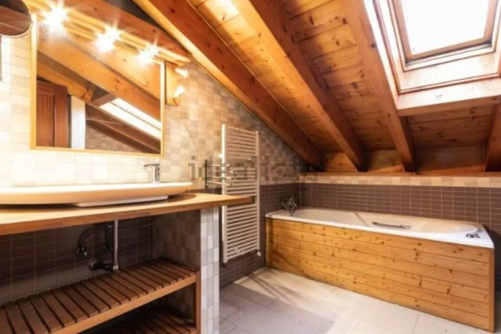 Baño con bañera de madera bajo el techo abuhardillado
