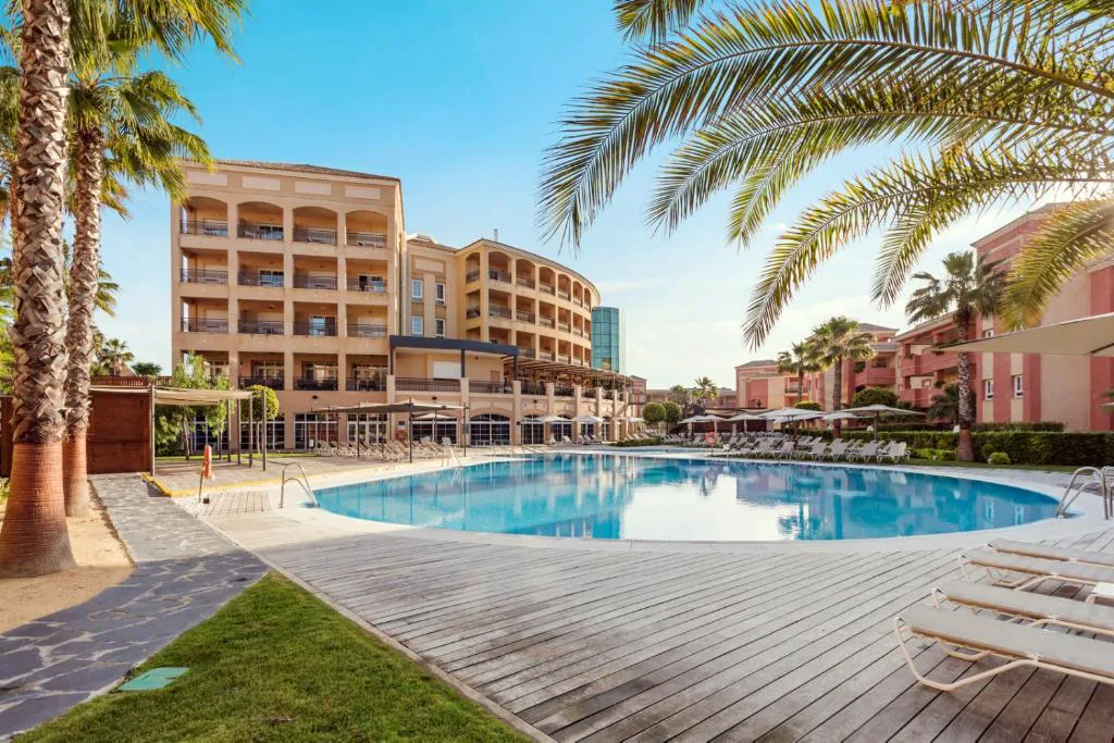 Piscina exterior con palmeras y el hotel al fondo