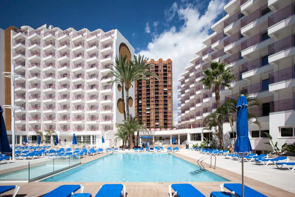 Piscina con tumbonas azules ante los edificios del hotel en Benidorm