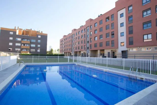 Piscina azul con césped junto a edificios de ladrillo