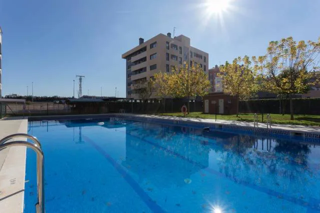 Piscina azul con césped y tumbonas junto a edificios