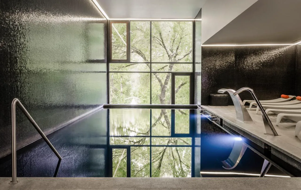 Piscina termal de mosaico oscuro con vistas al bosque en Aqua Village