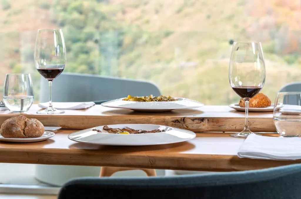 Mesa del restaurante puesta con vino y platos de cocina navarra frente a las vistas al valle