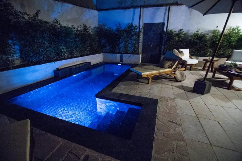 Piscina azul con luz nocturna en un patio con suelo de madera