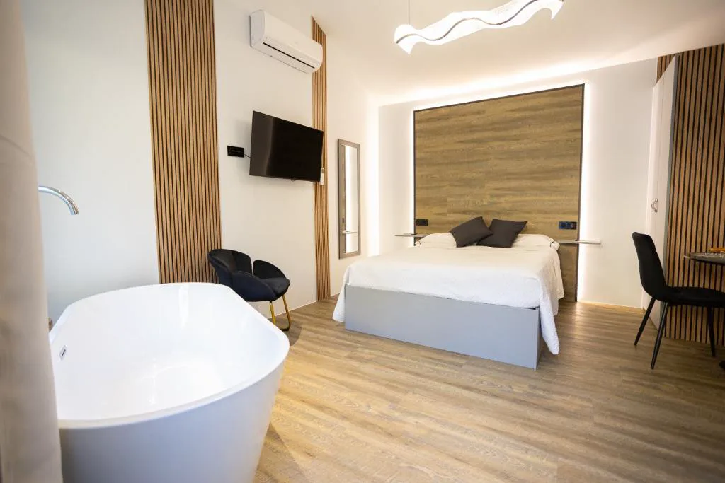 Bañera exenta junto a la cama con cabecero de madera iluminado, As Alvarizas