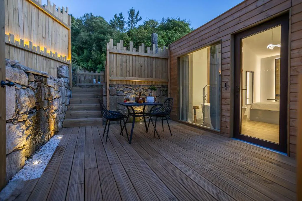 Terraza privada de madera con mesa y sillas al atardecer, muro de piedra iluminado, As Alvarizas