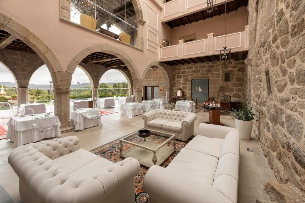 Salón con arcos de piedra, sofás blancos y vistas al patio, Áurea Palacio de Sober
