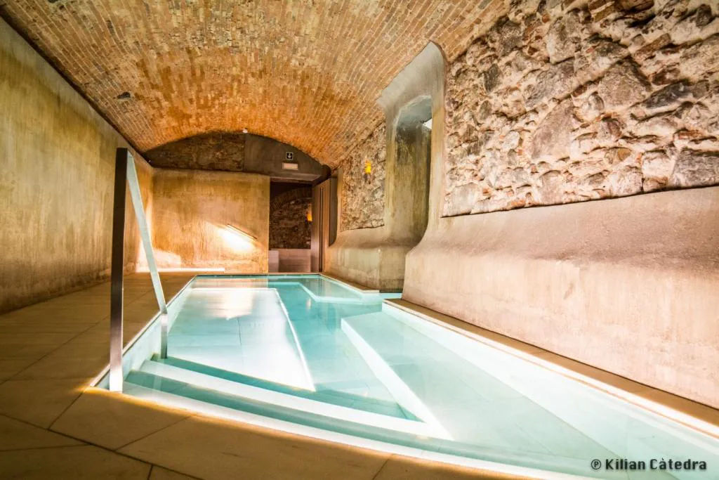 Piscina termal de suelo claro bajo un arco de piedra