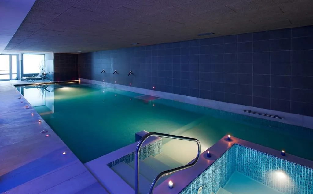 Piscina termal interior en tonos azules con escalera de acceso e iluminación ambiental