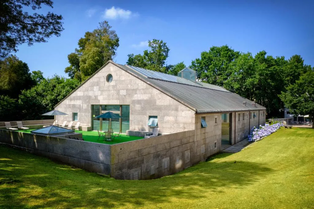 Edificio de piedra del spa con terraza y jacuzzi en azotea rodeado de jardín, Hotel Balneario de Compostela