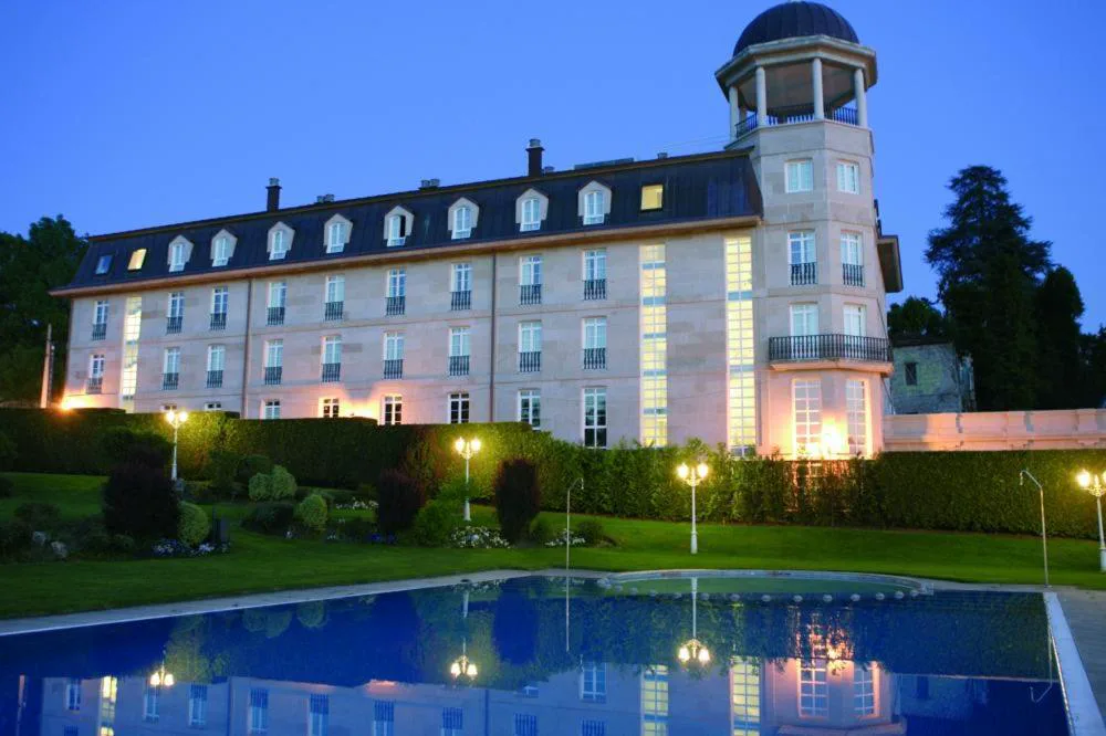 Fachada histórica del balneario iluminada al anochecer junto a la piscina exterior, Balneario de Mondariz