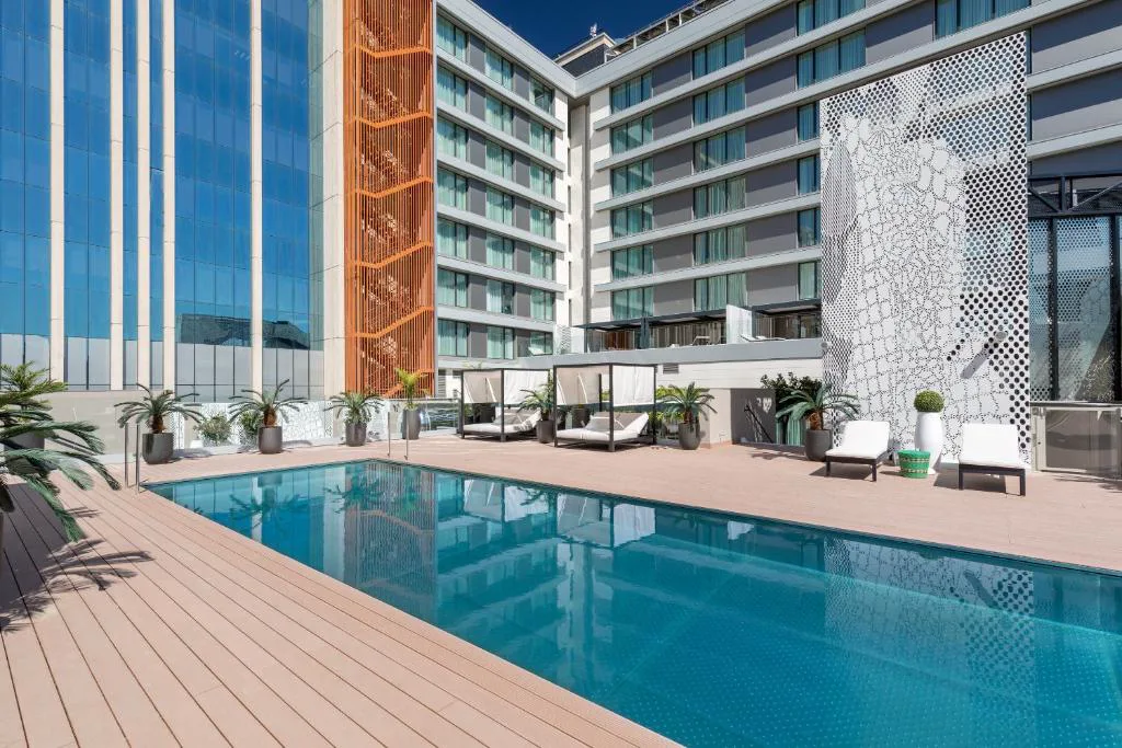 Piscina azul rodeada de tarima de madera junto a un edificio moderno