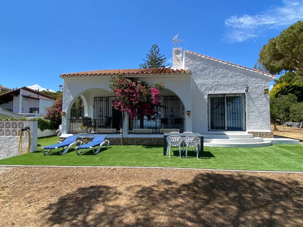 Villa blanca con jardín de césped y tumbonas bajo pinos