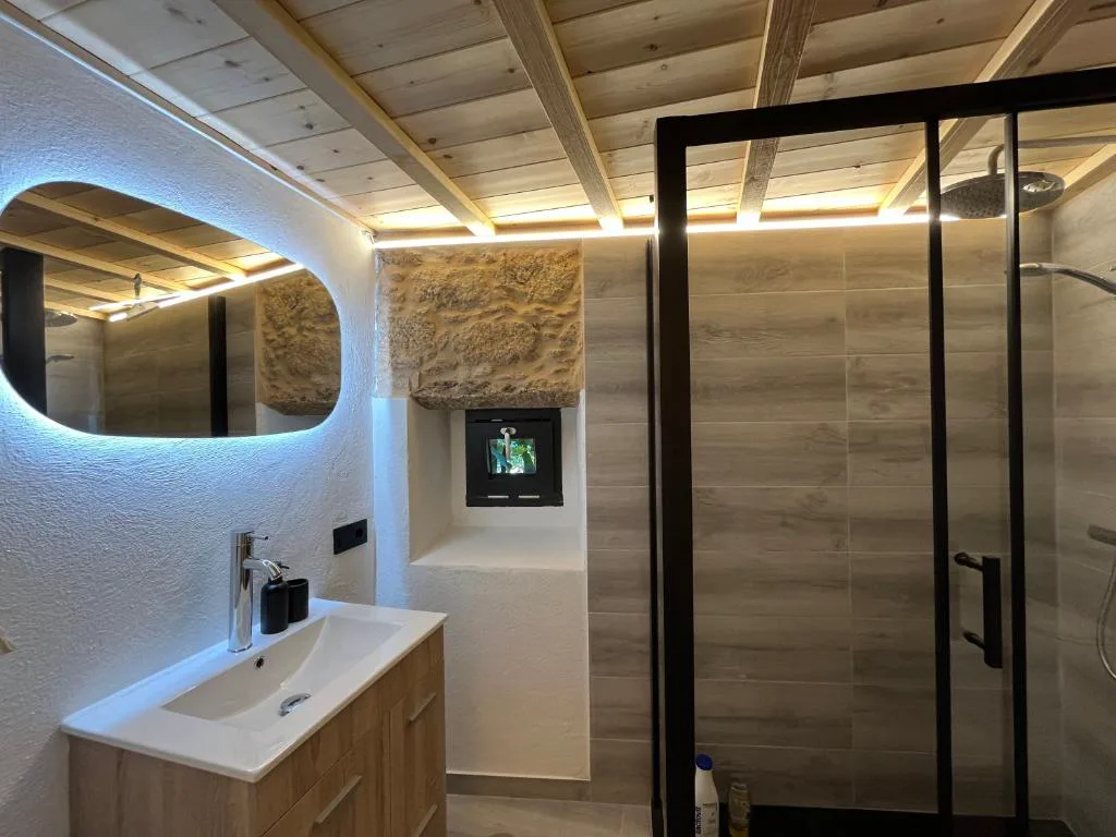 Baño de diseño con espejo ovalado retroiluminado y ventana a la chimenea de piedra, Bella Casa Araujo