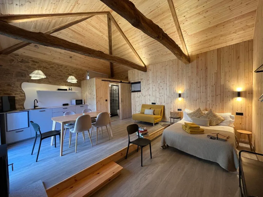 Loft abuhardillado con vigas de madera vista, cocina blanca y cama con sofá mostaza, Bella Casa Araujo