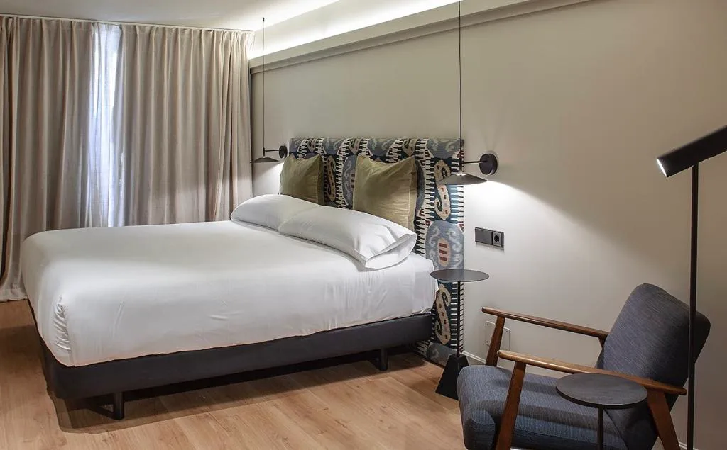 Habitación con cama grande de ropa blanca, sillón y ventana amplia