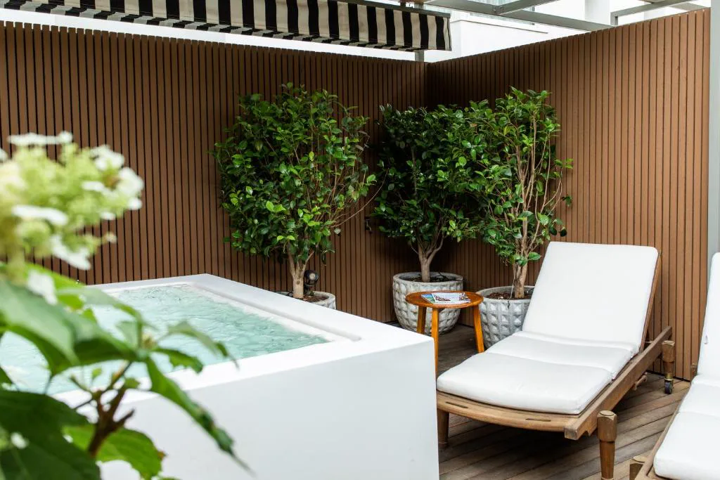 Rincón de la terraza con bañera blanca, tumbona y plantas entre paneles de madera