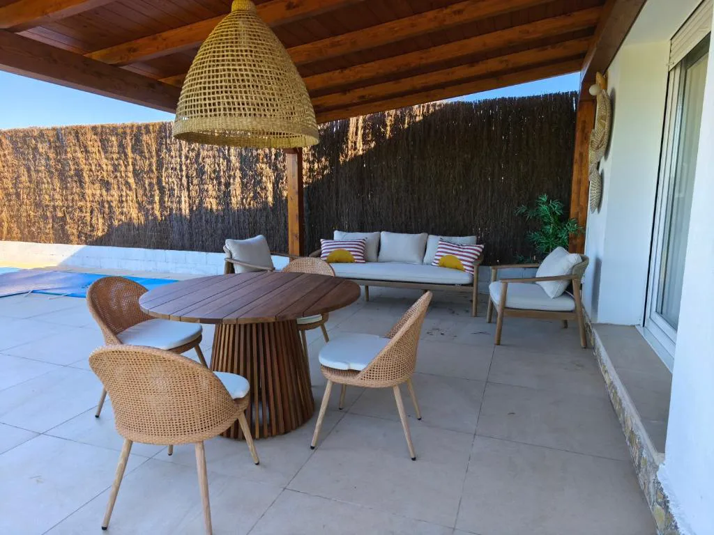 Terraza con mesa redonda de mimbre y sillones bajo un porche