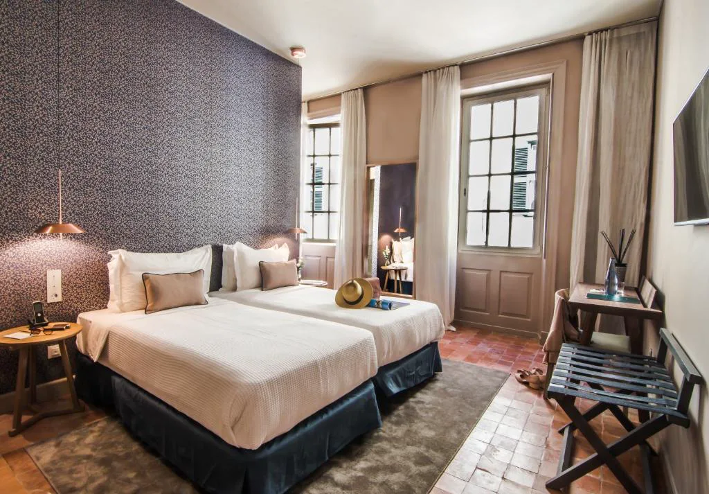 Dormitorio con papel pintado floral azul y sombrero sobre la cama, Bordoy Casa Ládico