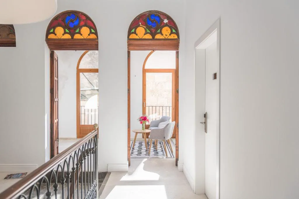 Pasillo con vidrieras de colores y puertas de madera abiertas al balcón, Bordoy Mostatxins