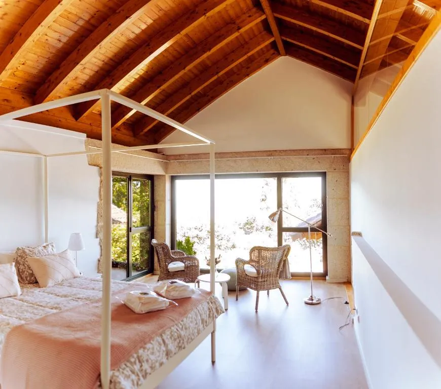 Dormitorio con cama con dosel de madera y grandes ventanales, en Bosque de Xarás