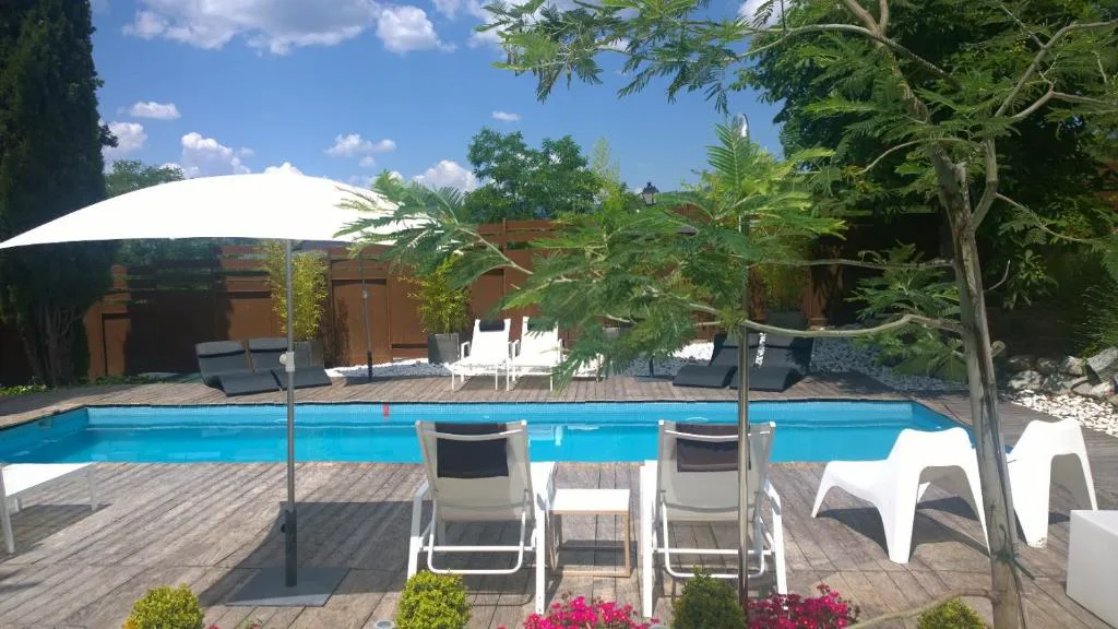 Piscina con tumbonas blancas y sombrilla entre los árboles