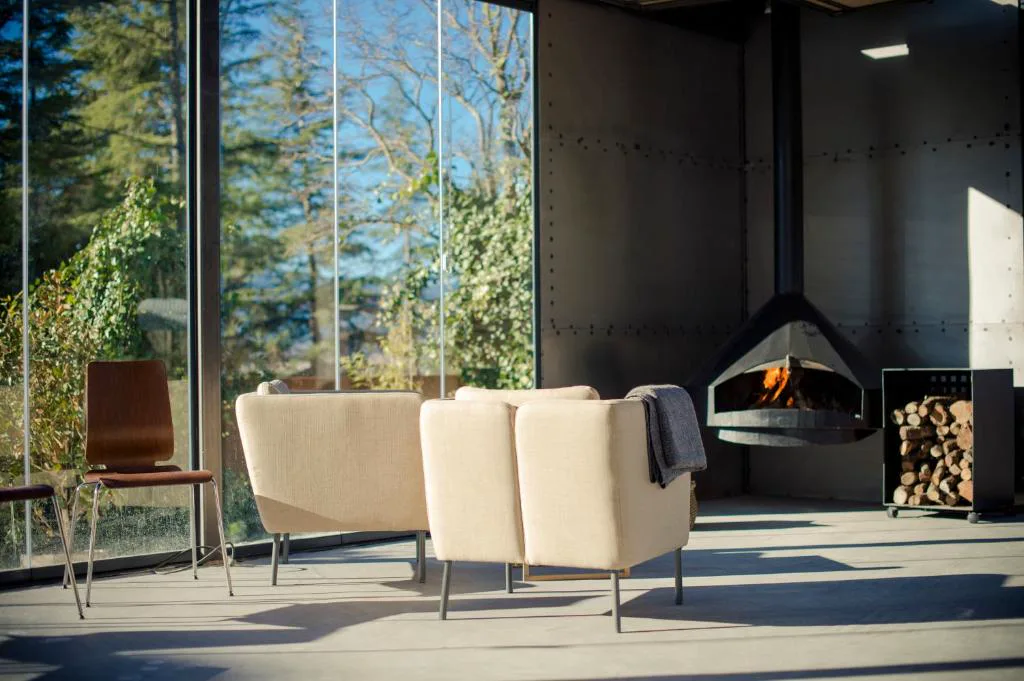 Salón con chimenea moderna y ventanal al bosque