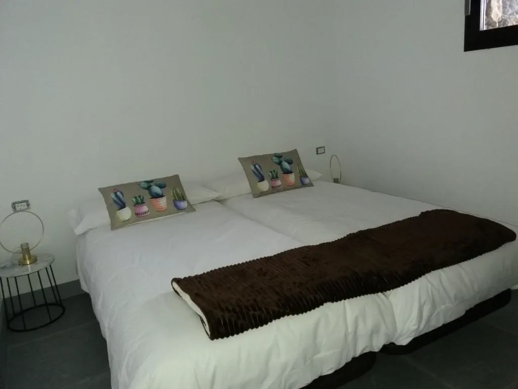 Dormitorio con cojines pintados de cactus sobre ropa de cama blanca, Bungalowmirador