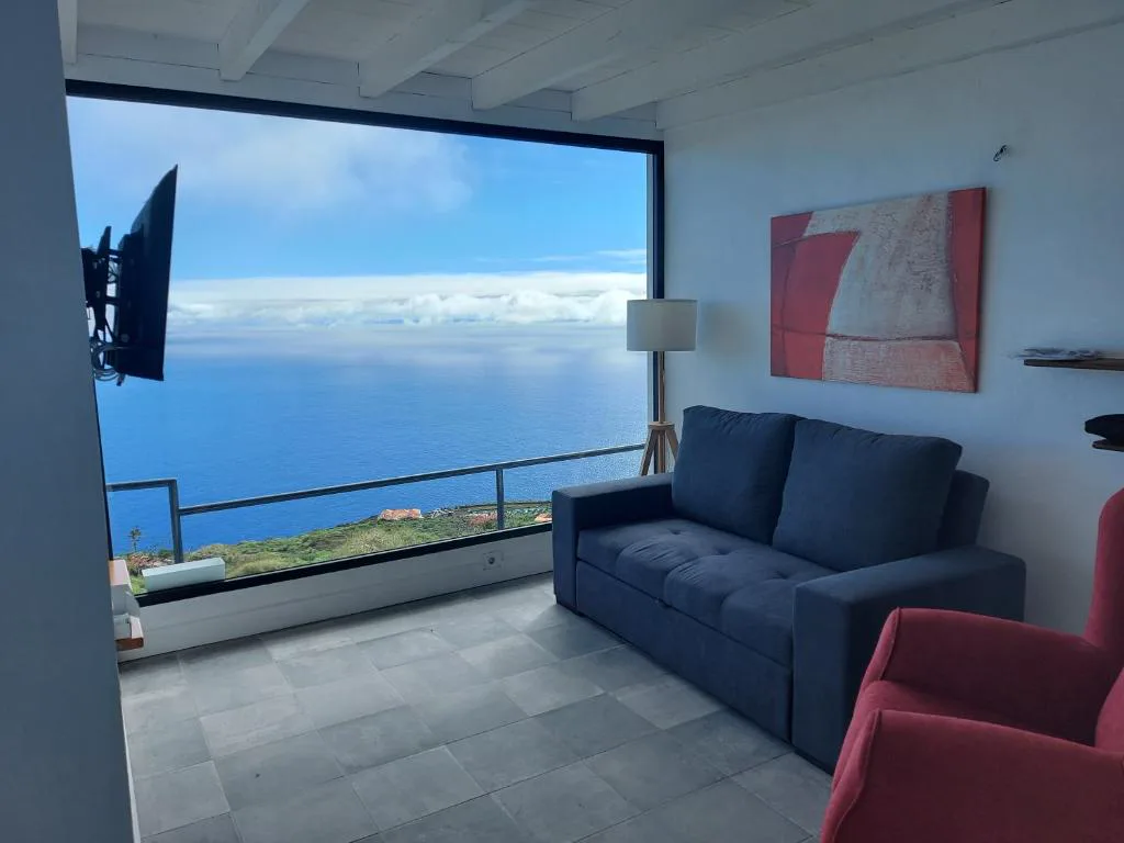 Salón con sofá azul y ventanal panorámico sin obstáculos al océano Atlántico, Bungalowmirador, Fuencaliente, La Palma