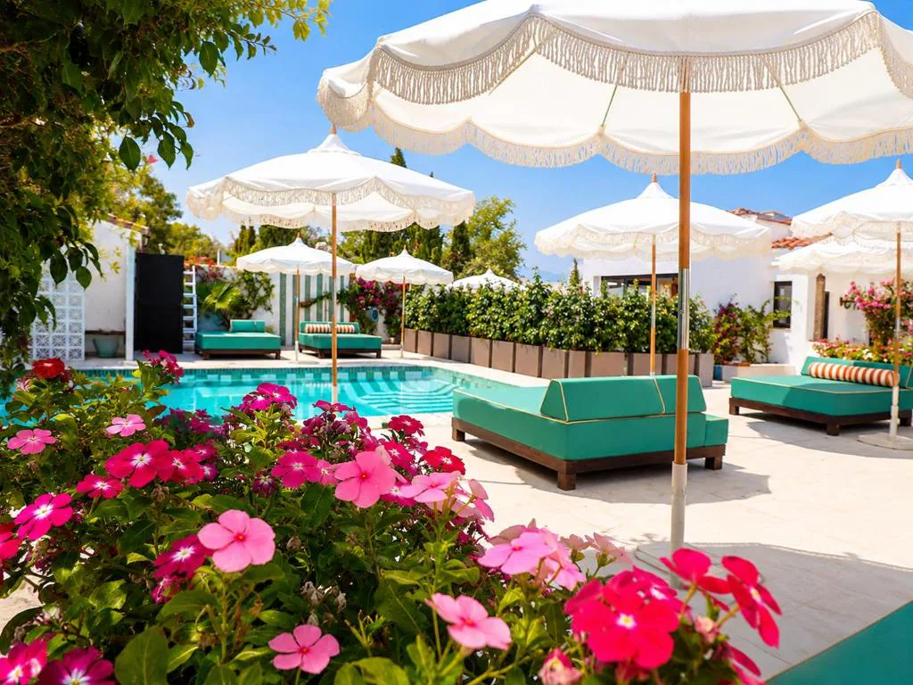 Piscina con sombrillas blancas, tumbonas verdes y flores rosas