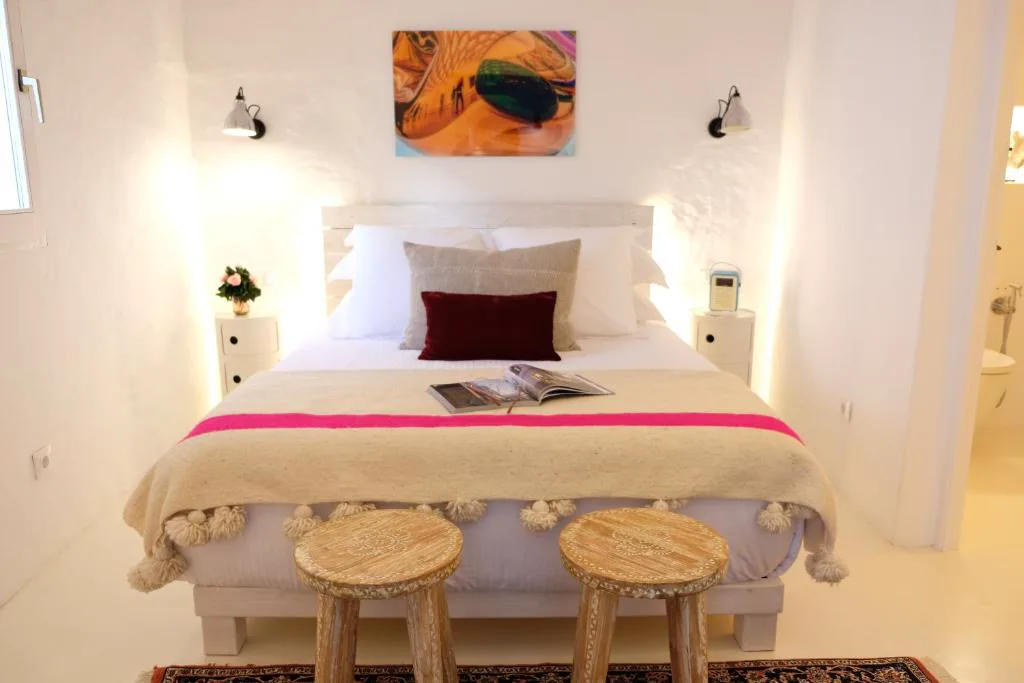 Dormitorio blanco con cabecero de madera clara y franja rosa en la colcha, Ca na Kika