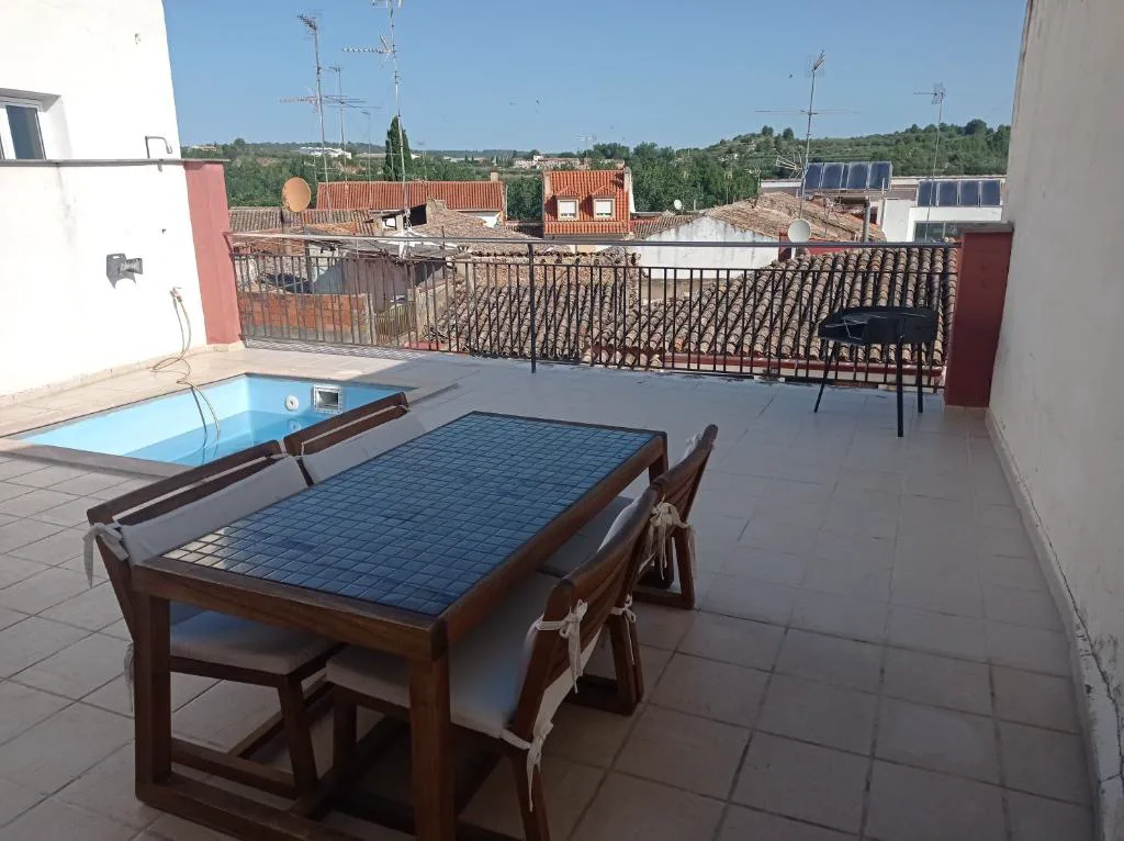 Terraza con mesa y piscina al fondo con vistas a los tejados del pueblo