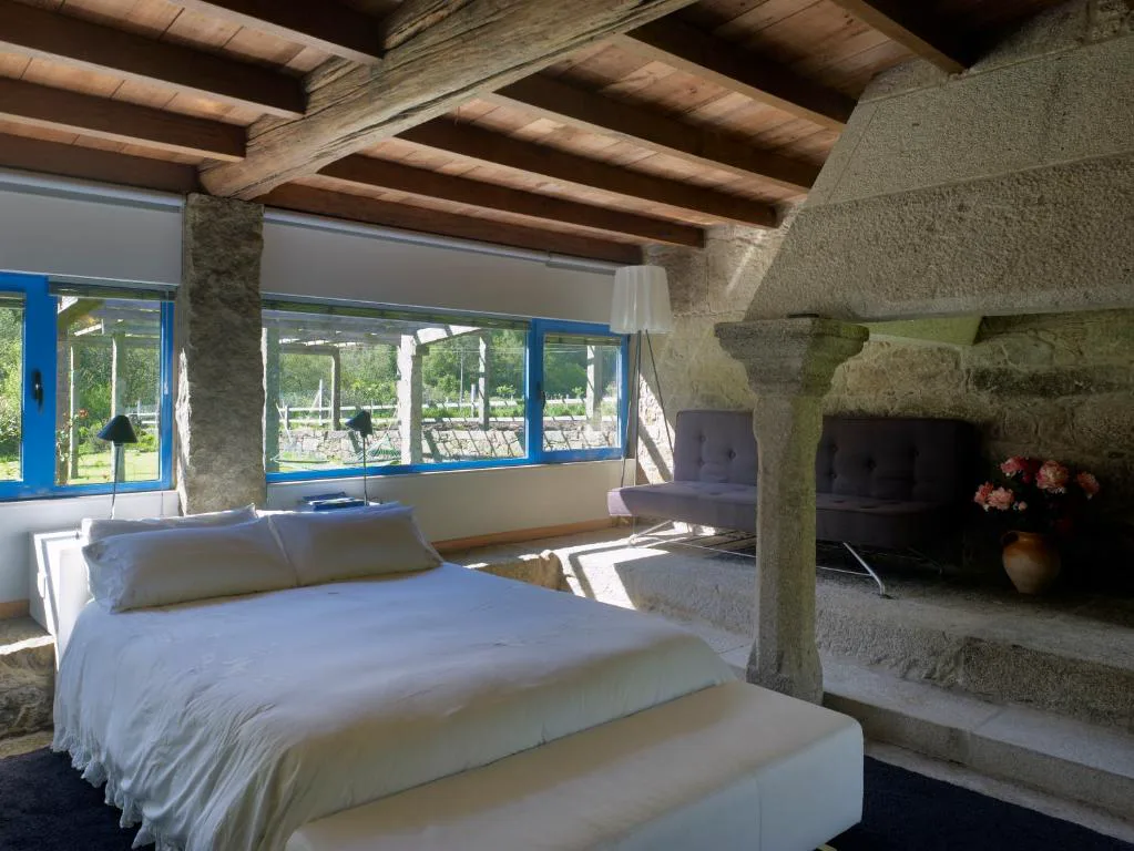 Dormitorio bajo una antigua lareira de piedra con columna de granito y vigas de madera vistas
