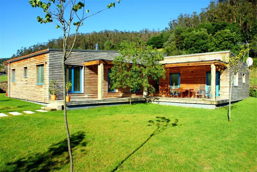 Fachada de la cabaña de madera con jardín y bosque de fondo, A Cabana de Carmen